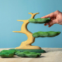 Close up of a hand removing the wooden leaves on the Bumbu handmade Bonsai tree toy on a wooden worktop in front of a blue background