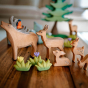 Bumbu plastic-free wooden deer toys stood on a wooden table next to some Bumbu small wooden grass and flower figures