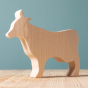 Bumbu Wooden Cow - Paint Your Own.  The toy sits on a wooden surface against a blue background.