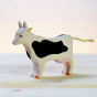 Bumbu handmade wooden black and white cow figure on a light wooden background in front of a white wall