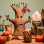 Bumbu Large Wooden Spooky Tree, a hand carved wooden toy in the shape of a spooky Halloween tree, posed in a Halloween play scene along with other spooky Bumbu toys such as a ghost and pumpkins.