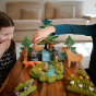 Two children playing with some Bumbu wooden animal figures on a wooden table next to the Waldorf grass and flower figures