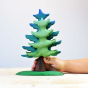 Hand holding the Bumbu plastic-free wooden spruce tree toy on a wooden worktop