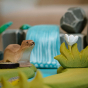 Close up of the Bumbu small wooden grass and white flower toy on a small world waterfall scene next to a wooden otter animal figure
