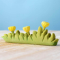 Bumbu large wooden grass toy with yellow flowers on a wooden worktop in front of a blue background