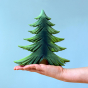 Bumbu Large Wooden Handmade Fir Tree in various shades of green, and a brown tree trunk being held in the palm of a hand with a blue background