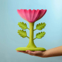 The Large Pink Flower by Bumbu is an impressive wooden flower with four leaves and a rich pink bloom, it stands on a green wooden base, with a blue background. An adults hand is shown for scale.