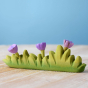 Bumbu large wooden grass toy with lilac flowers on a wooden worktop in front of a blue background