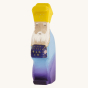 Bumbu Wooden Nativity Figure - Three Kings Melchoir on a cream background. Melchoir wears a purple and blue outfit and yellow crown, has a white beard and is holding a purple gift with gold details.