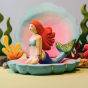 Photo of the Bumbu mermaid posed on top of the Bumbu wooden Clam Shell, in an aquatic ocean scene.