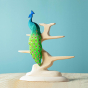 Bumbu plastic-free natural wooden bird tree with a Bumbu peacock figure balanced on top, in front of a blue background