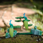 Close up of some Bumbu wooden peacocks and Bonsai tree toys on a mossy rock in front of a blurred beige background