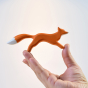 Close up of a hand holding the Bumbu childrens wooden running fox toy in front of a white background