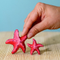 Bumbu Wooden Red Starfish Set next to a hand for size reference.
