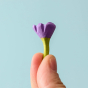 A small and delicate Bumbu Lilac flower being held between a persons finger tips on a light blue background