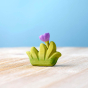 Bumbu handmade small wooden grass toy with lilac flower on a wooden worktop in front of a blue background