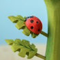 A bright red wooden ladybird with painted black spots, stood on a green leaf which is attached to a green plant stalk, on a light blue background