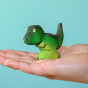 Wooden toy baby T-Rex in vibrant shades of green and purple. The baby T-Rex stands upright in a forward stance. The toy has painted eyes, claws, and body detail. The wooden figure sits on an adult hand to give a reference of scale.
