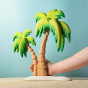 Bumbu Wooden Palm Tree. The toy sits on a wooden surface against a blue background. An adult hand is shown around the toy to denote the scale.