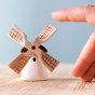 Bumbu Miniature Wooden Moldova Windmill. The toy sits on a wooden surface against a blue background. An adult hand is in view to show scale.