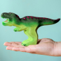 Wooden toy adult T-Rex in vibrant shades of green and purple. The T-Rex stands upright with its jaws open in a forward stance. The toy has painted teeth, claws, and eye detail. The figure is resting on an adult hand to show the scale of the item.