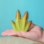 Bumbu Wooden Banana Bush pictured in an adults hand in front of a blue wall