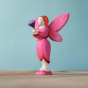 Bumbu Wooden Blossom Fairy. A Radiant and vibrant fairy figure holding a wooden purple flower in their hands. The Bumbu Blossom Fairy wear a bright pink painted dress with small red dot trim, bright pink wings with small red dots at the tips, pink shoes, 