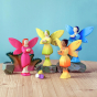 The four Bumbu Fairies together. From left to right is Blossom Fairy in pink, Woodland Fairy in Green, Sunflower Fairy in yellow/orange and Water Fairy in blue. The Fairies are stood on Bumbu rocks, on a wooden table with a blue background
