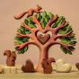 Squirrels happily play in and around The Bumbu Wooden Heart Tree with a light brown Bumbu wooden heart sitting in the heart cut out center, surrounded by white and brown Bumbu hearts, on a warm beige background