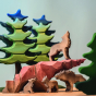 A Bumbu Howling Wolf is standing on top of the Bumbu Wooden Handmade Howling stone in rust red ombre colour, surrounded by Bumbu wooden trees. Below the Howling wolf stands a Bumbu angry wolf, a Bumbu wolf cub, and a Bumbu sitting cub