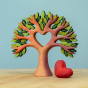 Bumbu Wooden Heart Tree. A beautifully crafted Wooden Tree with light brown branches, light and dark green leaves, a heart cut out in the middle, with a removable wooden red heart next to the tree. The tree is displayed on a wooden table with a blue backg