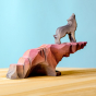 A Bumbu Howling Wolf is standing on top of the Bumbu Wooden Handmade Howling stone in rust red ombre colour, on a blue background. At the bottom of the Howlstone is a small cave