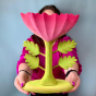 An adult holds the Bumbu Large Pink Flower in front of them. The Large Pink Flower by Bumbu is an impressive wooden flower with four leaves and a rich pink bloom, it stands on a green wooden base, with a blue background. An adults hand is shown for scale.