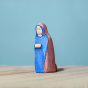 Bumbu Handmade Wooden Mary Figure kneeling down on a wooden table and blue background.