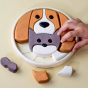 Wooden circular block puzzle with colourful pieces in various shapes forming an image of a cat and dog. Most of the puzzle is complete with three sections remaining to fill. There is an adult hand in the photo to show the scale of the puzzle. 