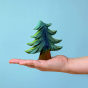 Bumbu Small Wooden Handmade Fir Tree in various shades of green, and a brown tree trunk being held in the palm of a hand with a blue background