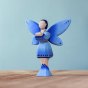 Bumbu Wooden Water Fairy Figure. The Water Fairy is coloured with hues of blue and silver on the wings, dress and boots, with inky blue hair, light blue eyes and pink lips. The Water Fairy is stood on a wooden table with a blue background