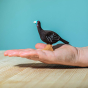 The Bumbu Turkey Hen is a beautiful eco-friendly wooden female turkey toy, hand carved and painted with a black body with white wing feather details, and a striking turquoise and red head. Adult hand for scale.