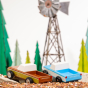 Candylab wooden pickup truck toys on some small stones in front of a metal wind turbine model