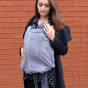Woman stood in front of a brick wall wearing the close caboo baby carrier fleece cocoon liner 