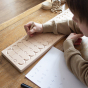 Child tracing over a Coach House handmade beech wood number line toy on a wooden table