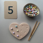 The Coach House Heart Fine Motor Board, a number '5' card, tweezers and a bowl of pompom loose parts. 