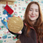 Close up of woman holding up the Divine giant Fairtrade milk chocolate coin in front of a white patterned wall