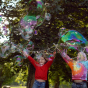 Children holding up the Dr Zigs jumbo bubble wands and letting bubbles fly up into the trees
