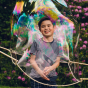 Boy stood smiling inside a giant Dr Zigs outdoor bubble in front of some pink flowers