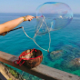 Close up of some hands holding up a giant bubble in the Dr Zigs bubble wand above a coconut bucket