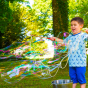 Young boy blowing a giant eco-friendly Dr Zigs bubble in front of a tall tree