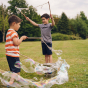 Two children in a park making bubbles with the Dr Zigs Multi-Loop Bubble Wand with trees in the background