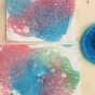 Close up of some blue, pink and green bubbles, blown onto sheets of white paper