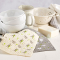 Ecoliving compostable home cleaning cloths laid out on a white table next to a stack of white bowls and kitchenware